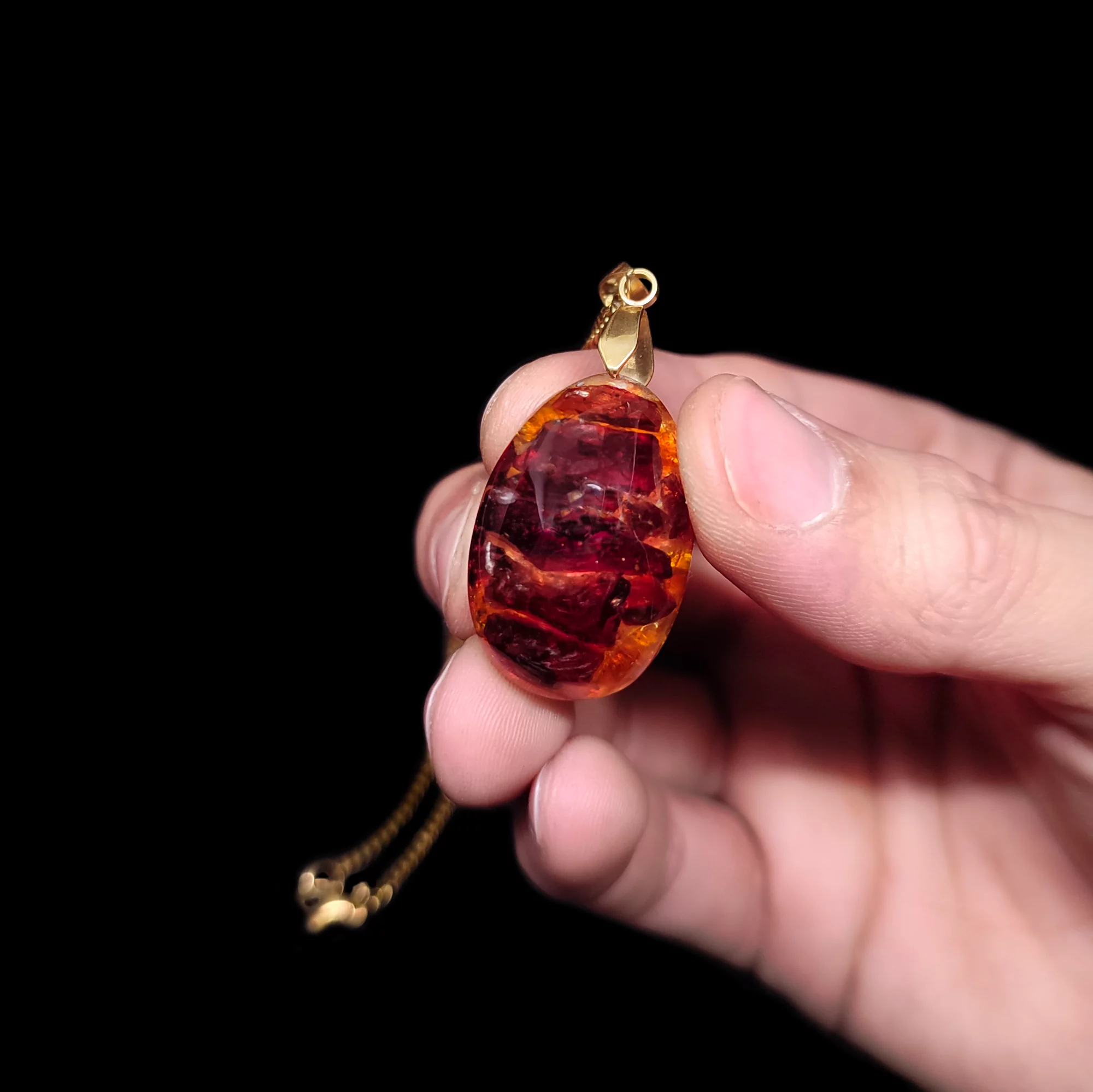 Produktpräsentation eines rot orangenen Orgonit Schmuckstück. Der Anhänger ist an einer vergoldeten Kette befestigt.
