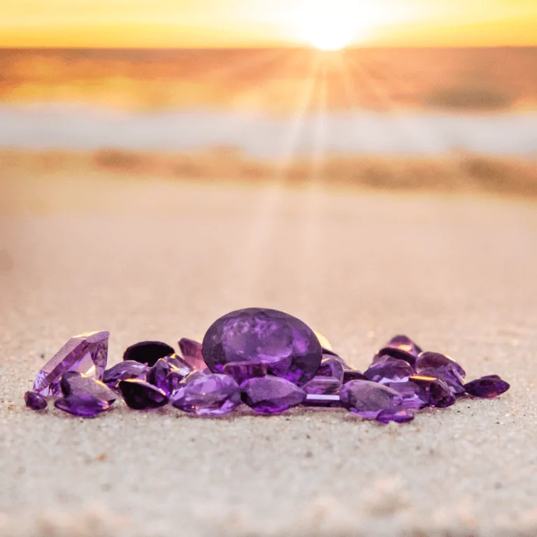 Facettierte Amethyst Edelsteine in mehreren Formen, welche am Strand liegen. Symbolbild für unseren Blog-Beitrag über die Bedeutung des Amethysten.