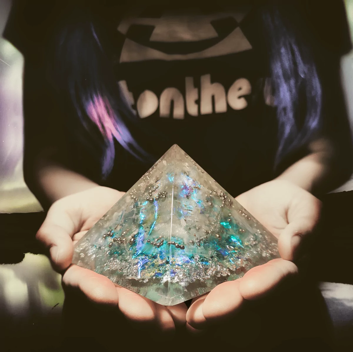 Orgonit Pyramide in Frauenhänden mit Polarlicht Hintergrund. Die Frau trägt ein firstonthesun T-Shirt.