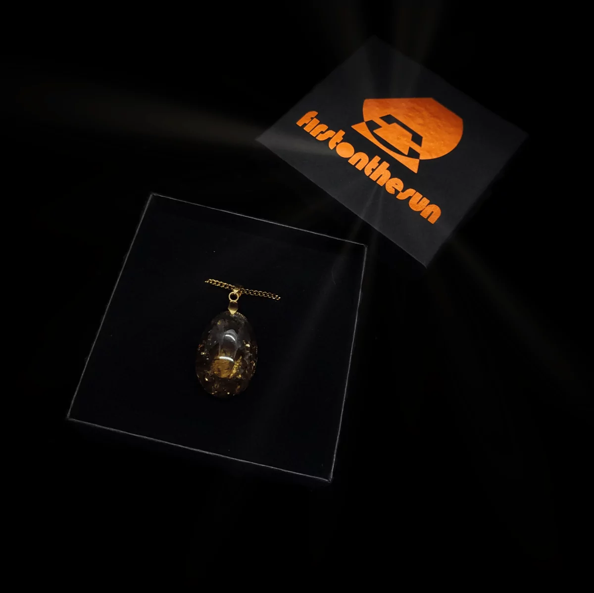 Edelstein Orgonit Anhänger mit einem firstonthesun Schmuckkarton. Das Schmuckstück ist grau/golden, während der Karton metallic orange bedruckt ist.