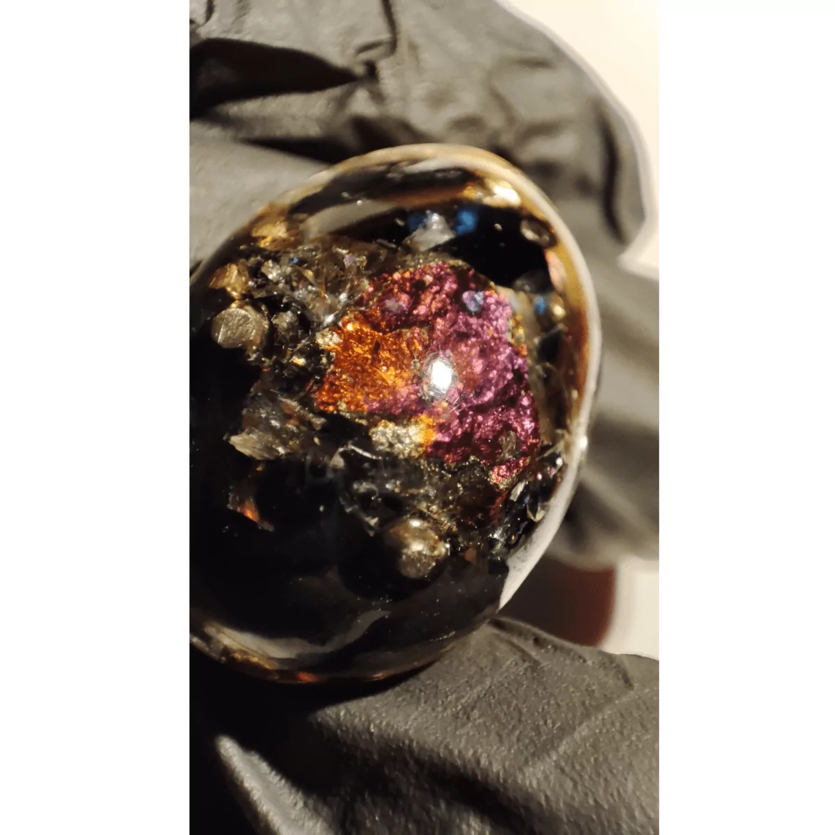Ein Orgonit Schutz Amulett mit Bornit als Nahaufnahme. Der Anhänger ist primär schwarz, golden und weist einen regenbogenfarbenen Stein auf.