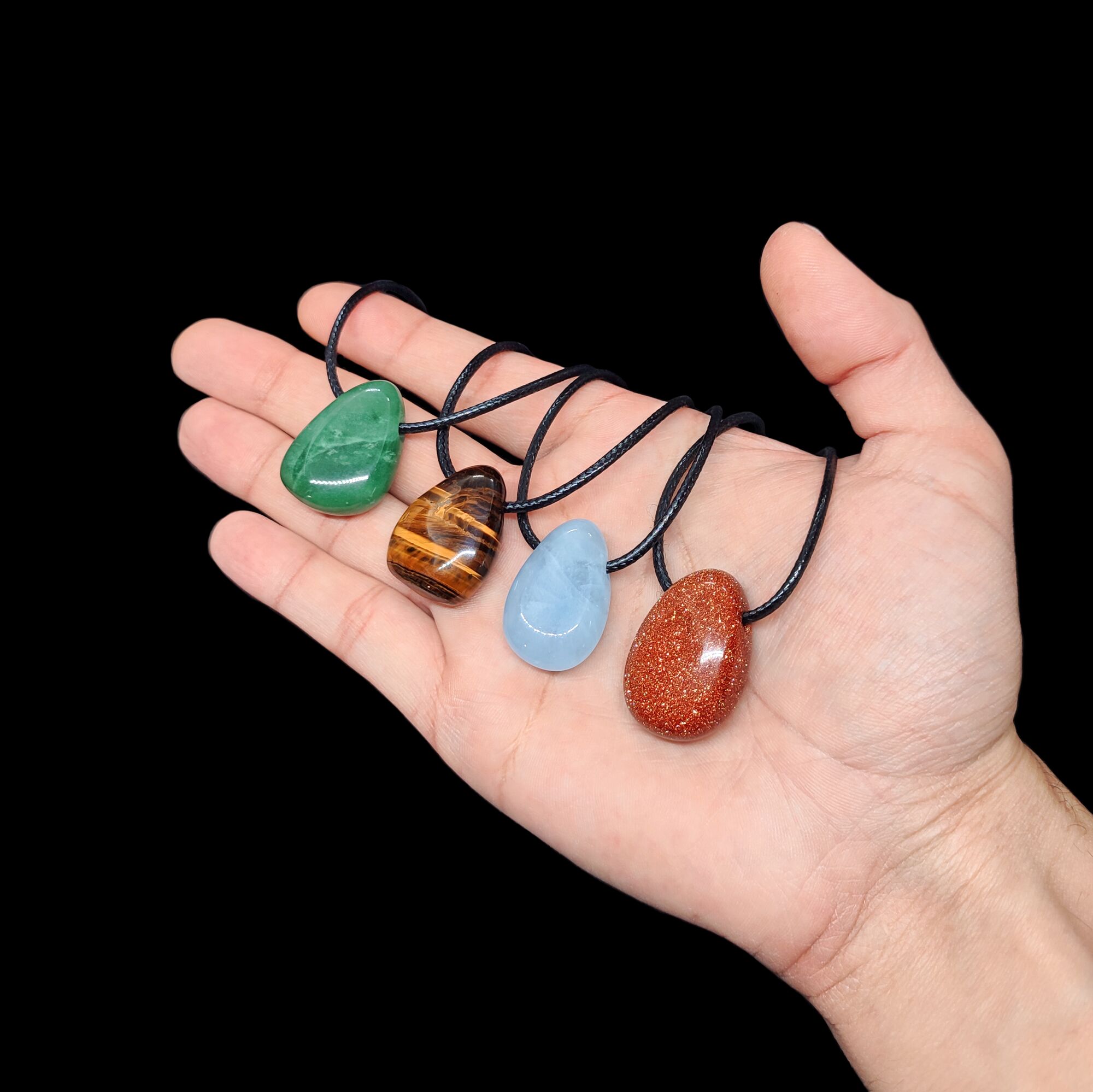 Aventurin, Tigerauge, Aquamarin & Blaufluss Edelstein Tropfen-Anhänger auf einer Handfläche.
